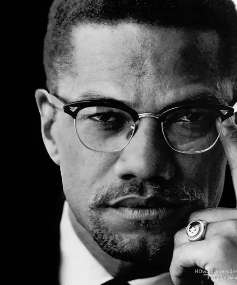 Malcolm X — black and white portrait, glasses raised to temple, c. 1964